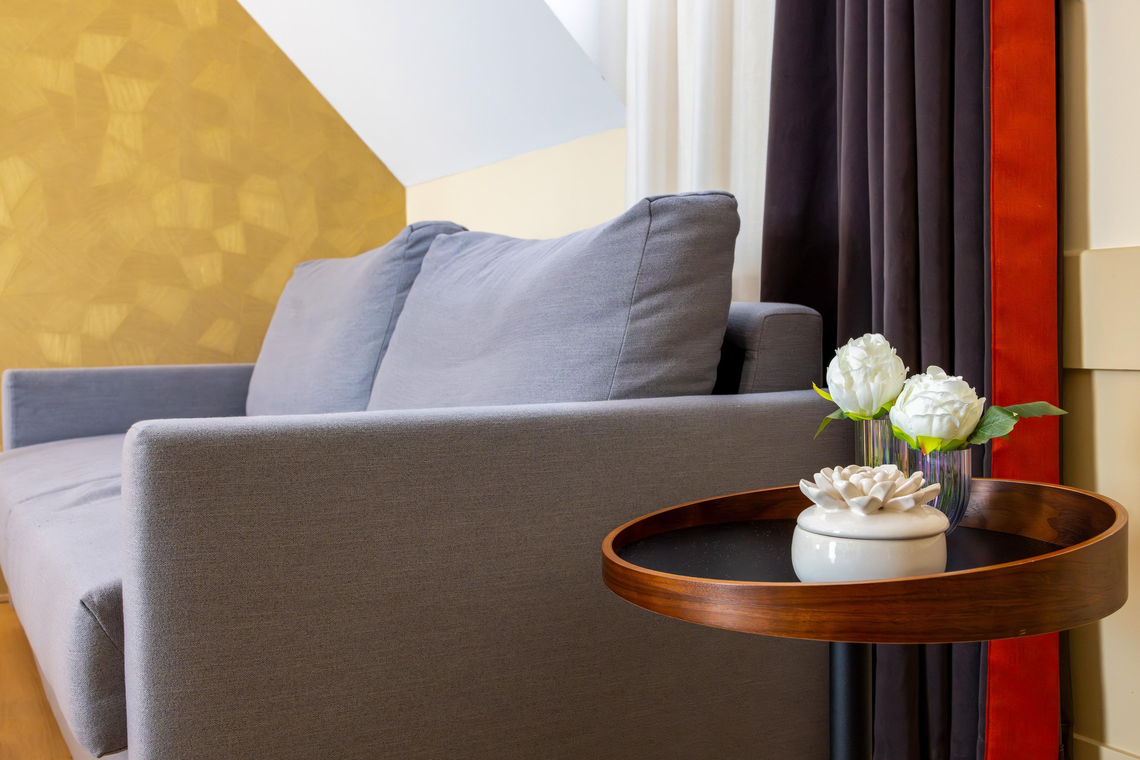 Una sala de estar moderna con un sofá gris, una mesita de madera con un florero blanco con flores, y un jarrón con flores blancas.