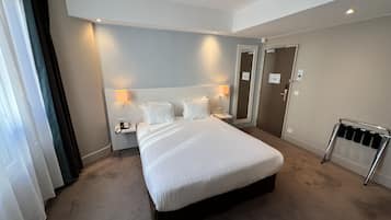 A hotel room with a large bed, bedside lamps, a telephone, and a radiator.