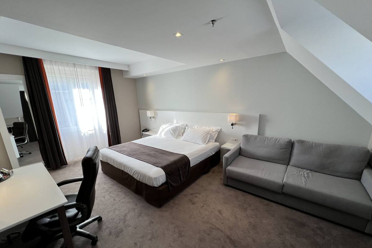 A modern hotel room with a large bed, a sofa, a desk, and a chair.