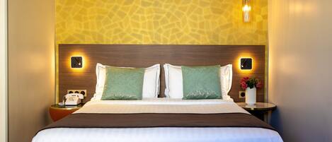 A hotel room with a large bed, two bedside tables, a telephone, and a wall-mounted light fixture.