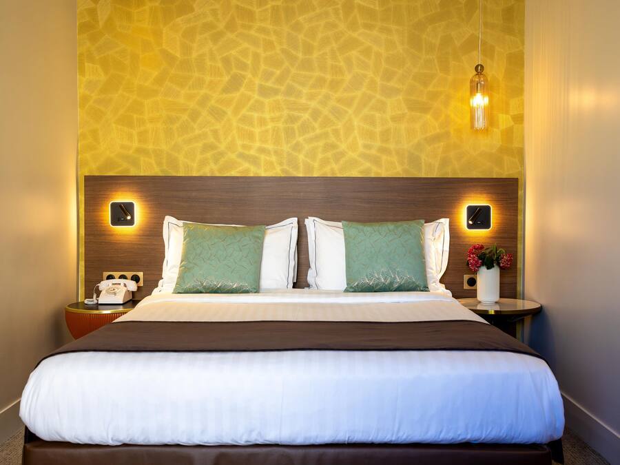 A hotel room with a large bed, two bedside tables, a telephone, and a wall-mounted light fixture.