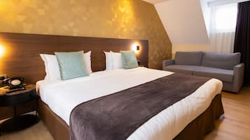 Una habitación de hotel con una cama grande, un sofá, una mesita de noche con teléfono e iluminación de pared.