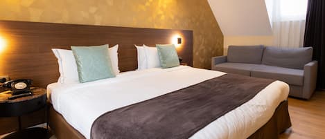 Una habitación de hotel con una cama grande, un sofá, una mesita de noche con teléfono e iluminación de pared.