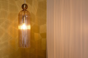 A pendant light fixture with a clear glass shade and a metallic base, hanging from a ceiling with a geometric patterned wall.