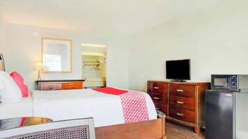 A hotel room with a bed, a dresser, a television, and a refrigerator.