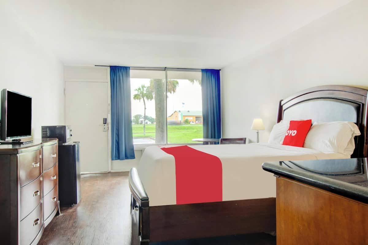 Une chambre d’hôtel avec un lit, une télévision, un bureau et une fenêtre avec des rideaux.