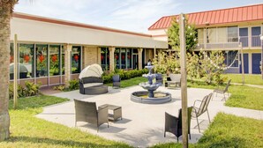 A courtyard with outdoor seating, a fountain, and a building with large windows and a red roof. - OYO Hotel Dundee By Crystal Lake (Dundee)