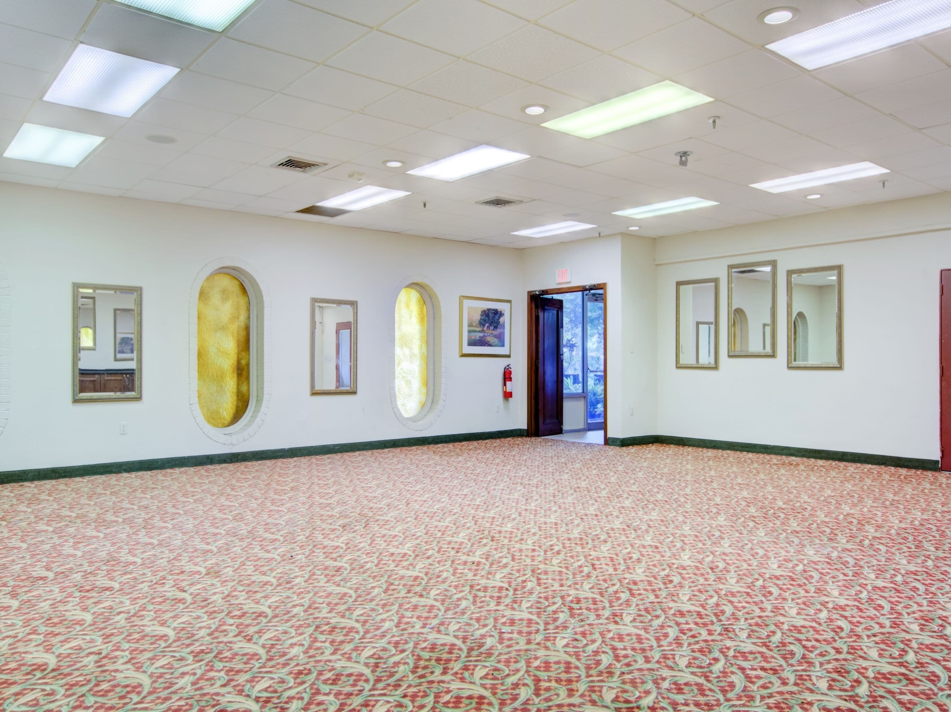 A spacious hallway with patterned carpet, multiple framed artworks on the walls, and a door leading to another room.