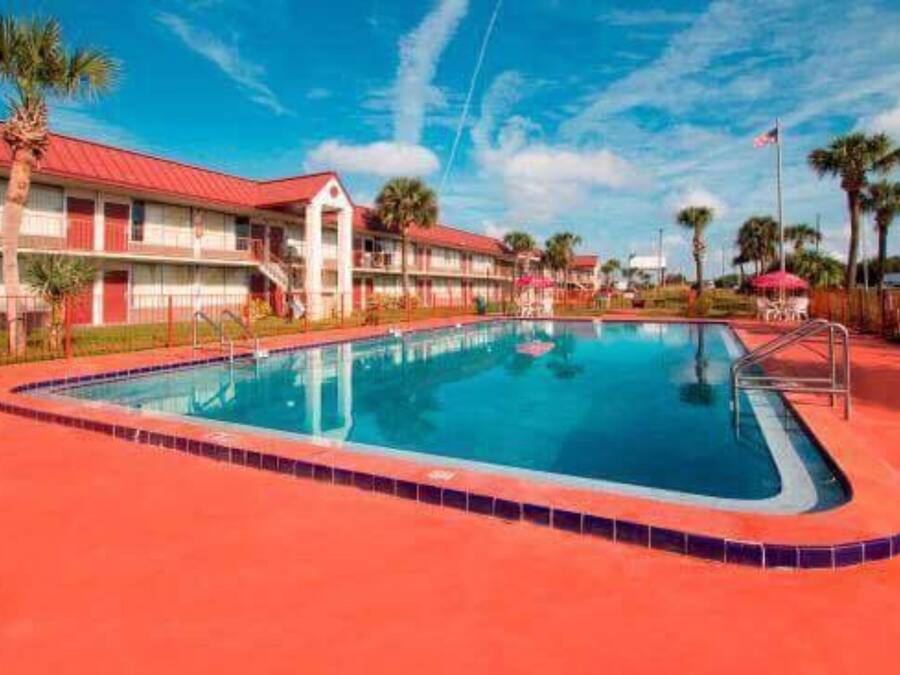 A motel with a swimming pool, palm trees, and a red-roofed building.