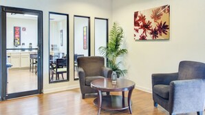 A spacious room with a wooden floor, a round table, two armchairs, a potted plant, and a large floral painting on the wall. - OYO Hotel Dundee By Crystal Lake (Dundee)