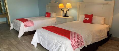 Dos camas individuales con ropa de cama blanca y detalles rojos, una mesita de noche con dos lámparas y un espejo en la pared izquierda.