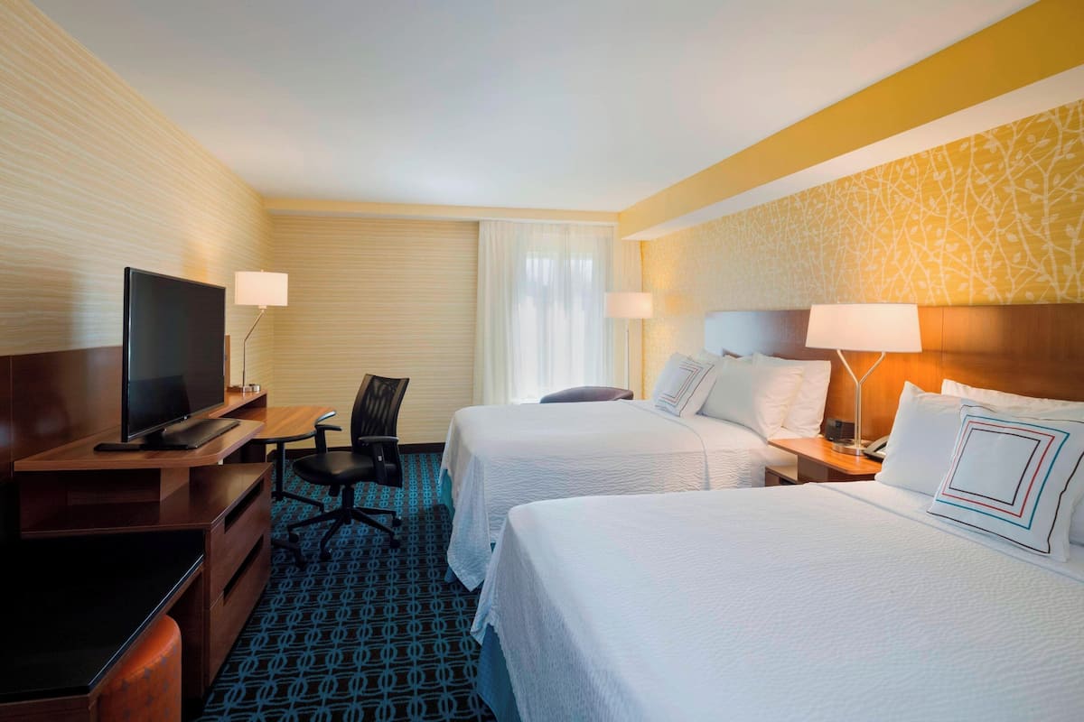A hotel room with two beds, a desk with a TV, a chair, and a lamp.