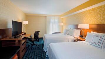 A hotel room with two beds, a desk with a TV, a chair, and a lamp.