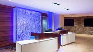 A reception area with a modern design, featuring a reception desk, a decorative wall with blue lighting, and a stone accent wall. - Fairfield Inn & Suites by Marriott Paramus (Paramus)