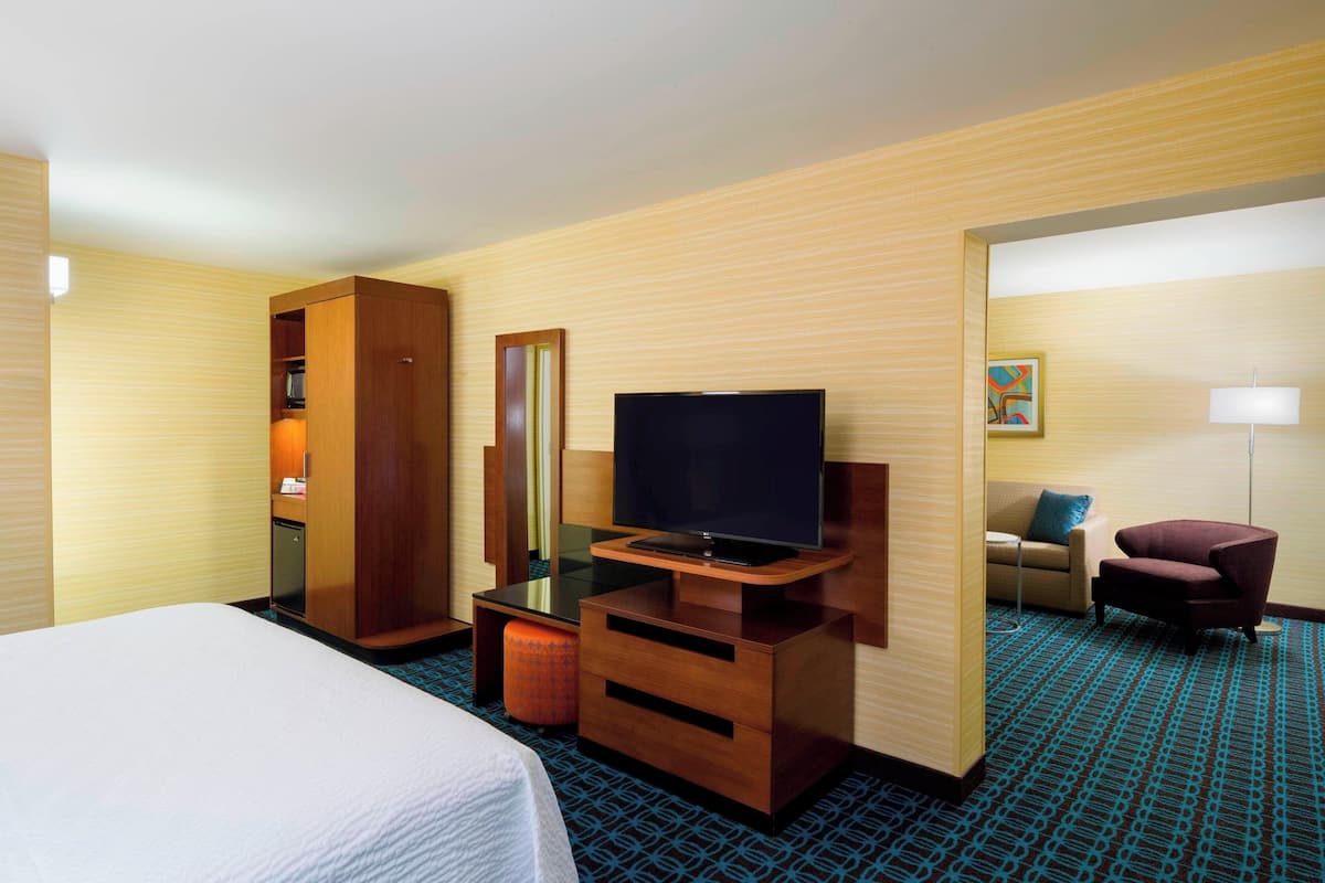 A hotel room with a bed, a TV on a wooden stand, a wardrobe, a sofa, and a patterned carpet.