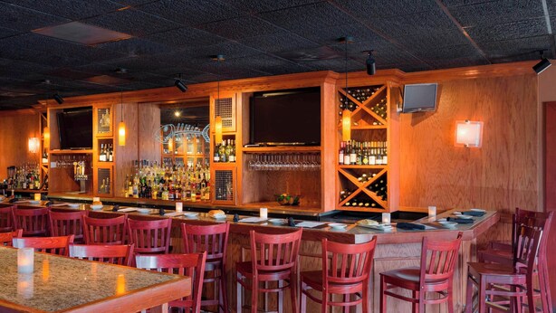 A bar area with wooden bar counters, red bar stools, and a variety of bottles and glasses. - Fairfield Inn & Suites by Marriott Paramus (Paramus)