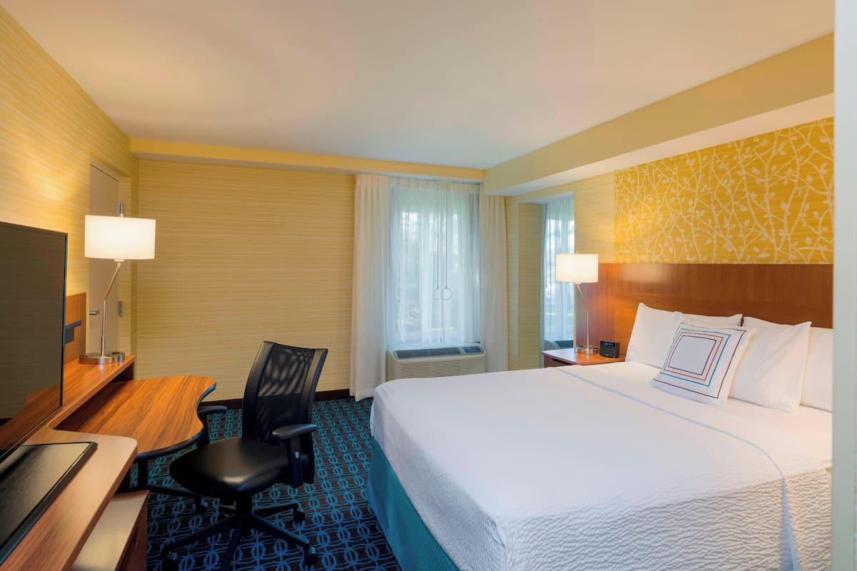A hotel room with a bed, desk, chair, and a TV.