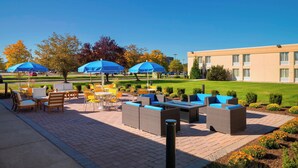 An outdoor patio area with wicker furniture and blue umbrellas, a lawn, and a building in the background. - Fairfield Inn & Suites by Marriott Paramus (Paramus)