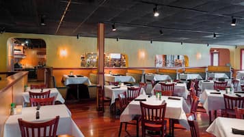 A restaurant with multiple tables and chairs, a bar area, and a view of the kitchen.