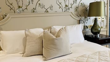 A neatly made bed with white linens and beige pillows, a green lamp on a bedside table, and floral wallpaper on the wall.