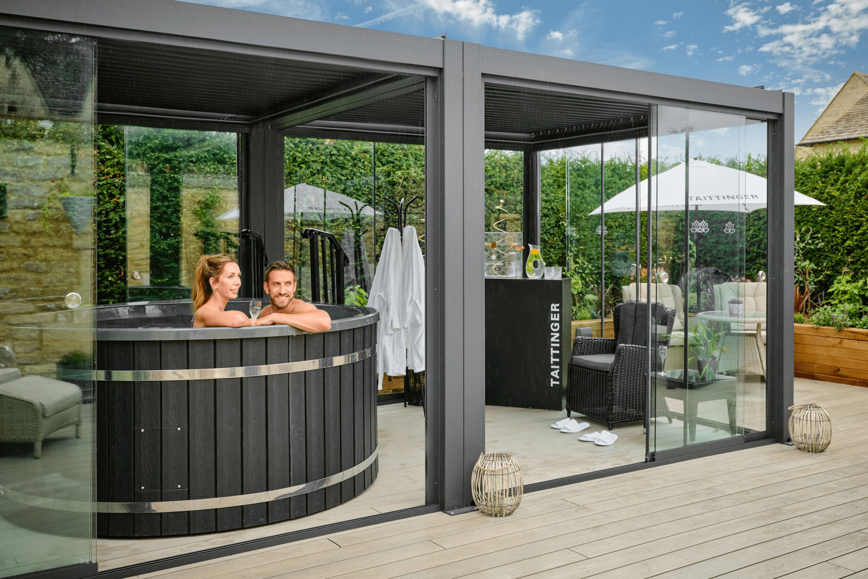 Un área moderna al aire libre con jacuzzi, paredes de vidrio, zona de estar y el nombre de la marca 'TAITTINGER' a la vista.