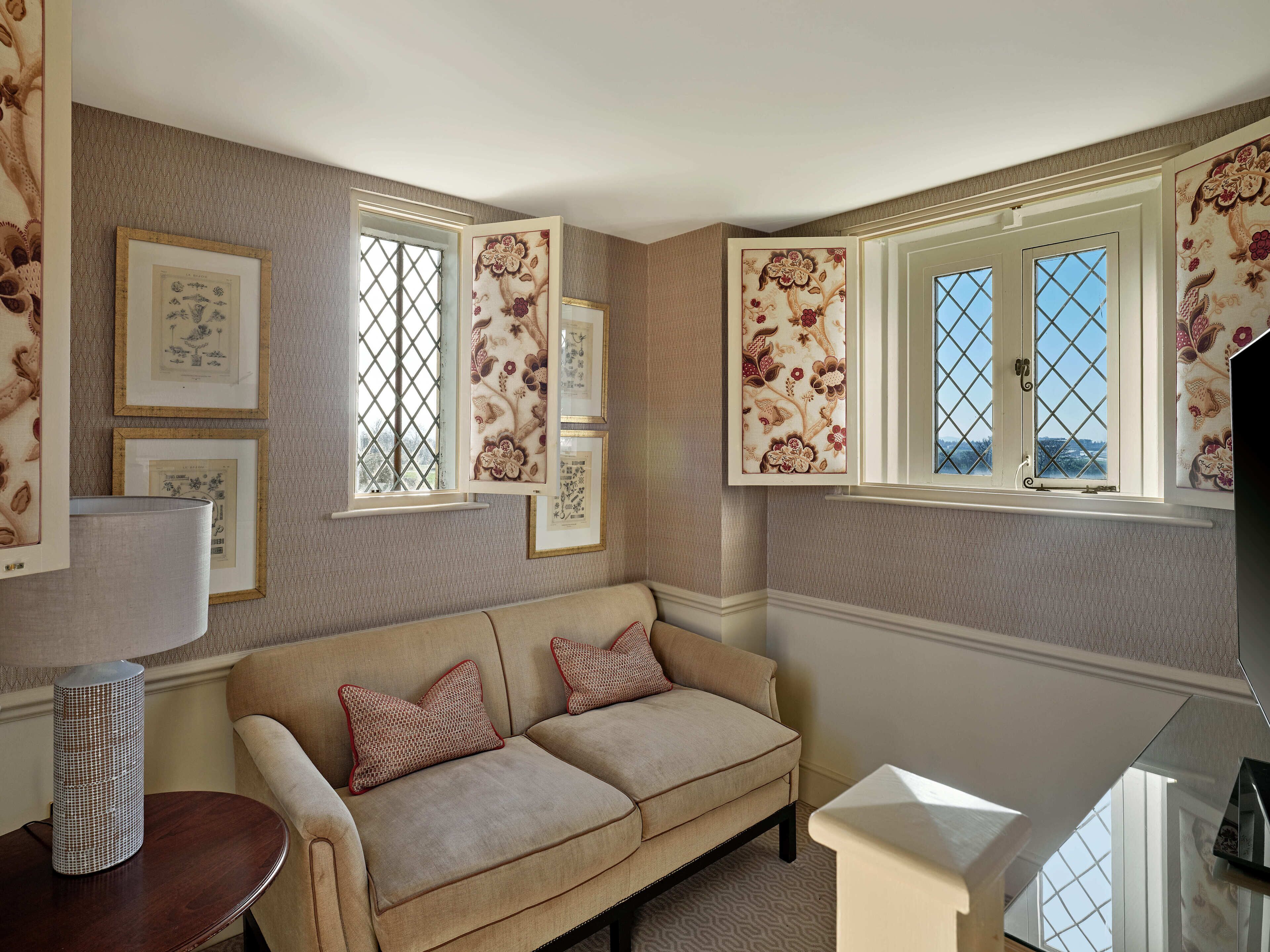 A cozy room with a beige sofa, two pillows, a lamp, and framed botanical prints on the wall.