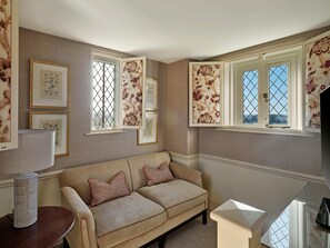 A cozy room with a beige sofa, two pillows, a lamp, and framed botanical prints on the wall. - Ellenborough Park (Cheltenham)