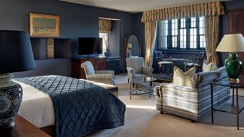 A hotel room with a large bed, two armchairs, a sofa, a small table, a TV, and a window with curtains.