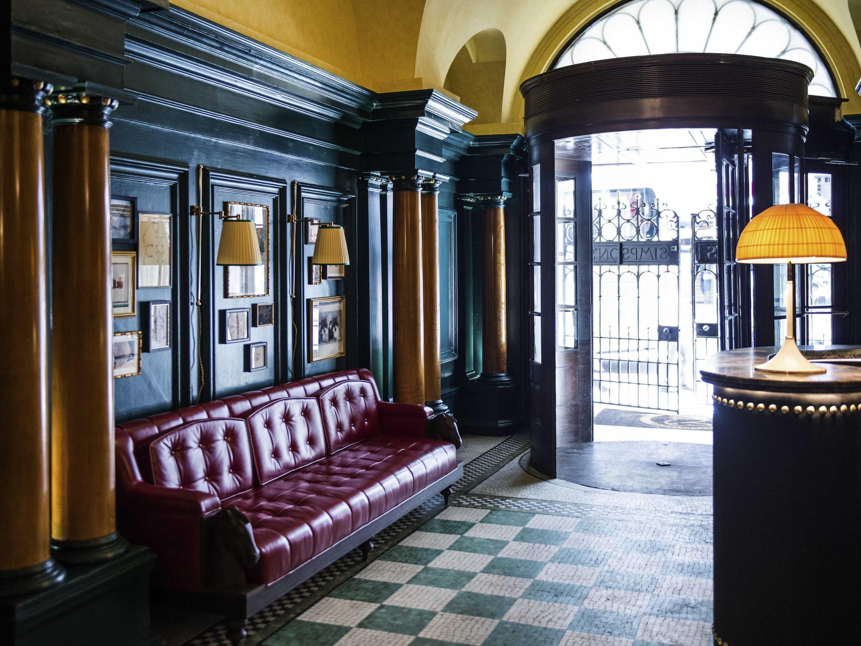 A lobby with a red leather sofa, framed pictures on the wall, and a checkered floor.