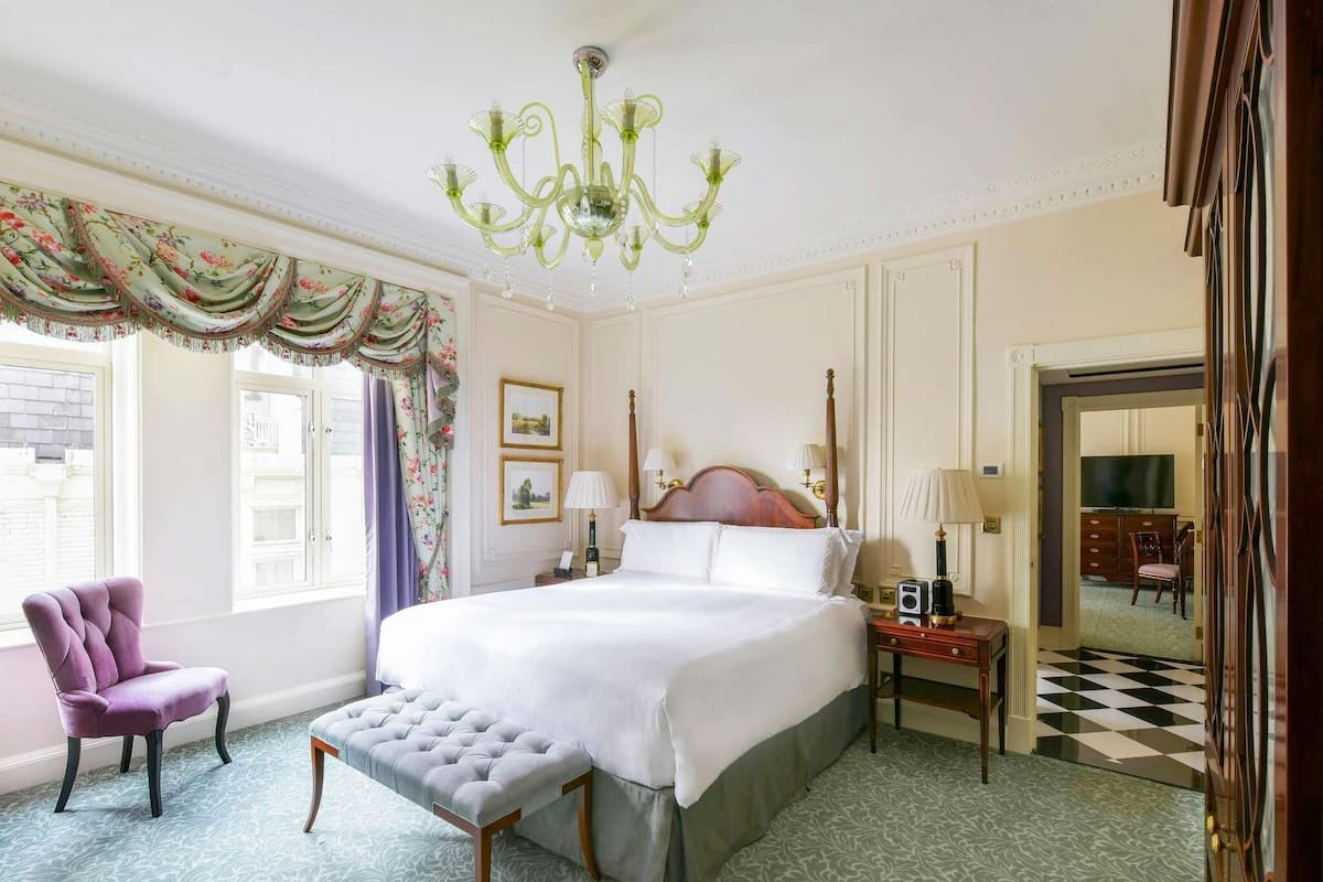 Ein Hotelzimmer mit einem großen Bett, einer Kristallleuchter, einem Schminktisch mit Spiegel und einem Schachbrettfußboden.