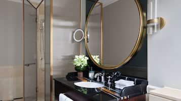A modern bathroom with a glass shower enclosure, a large round mirror, and a marble vanity.