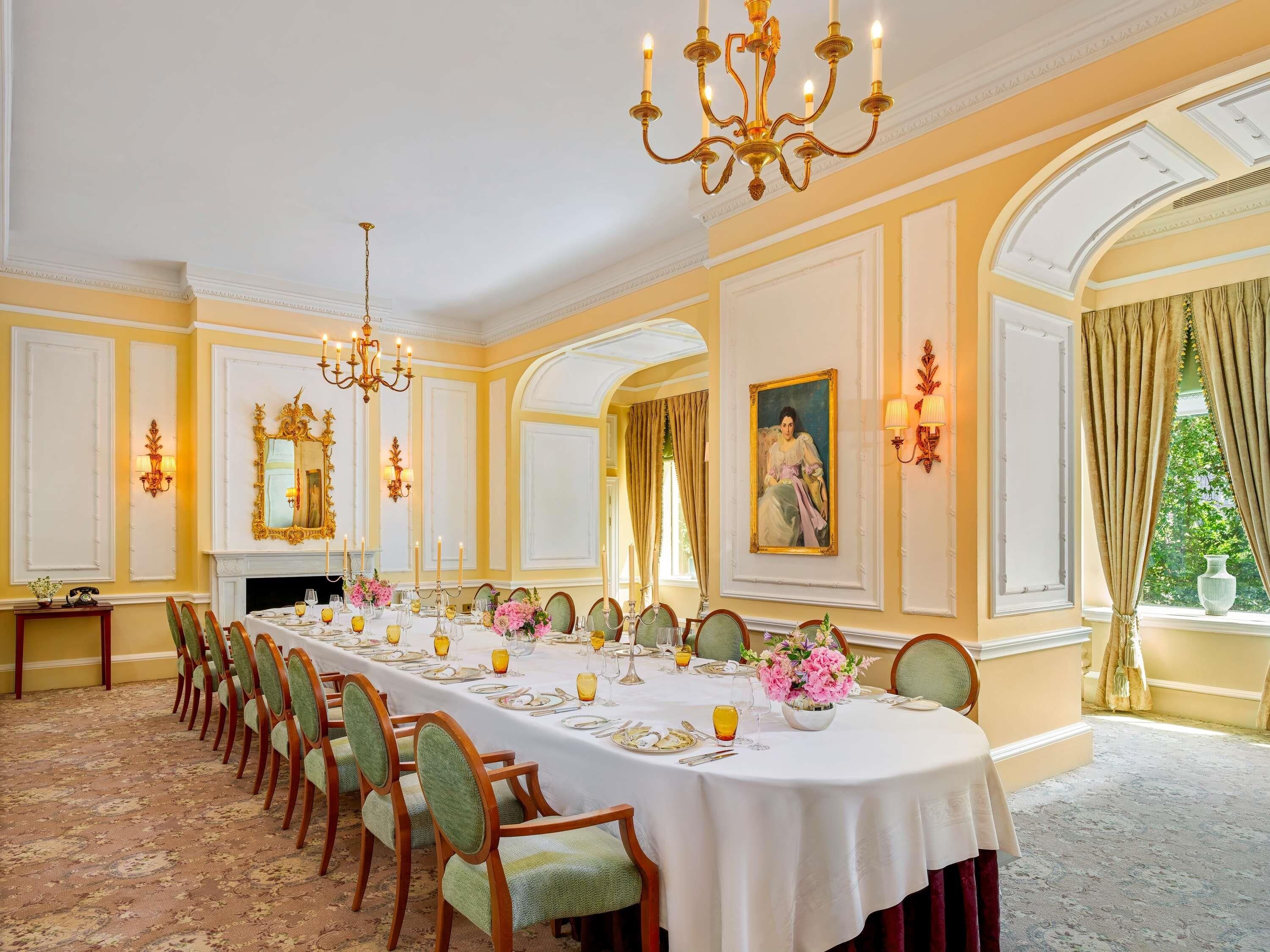 A formal dining room with a long table set for a meal, elegant chandeliers, and classic decor.