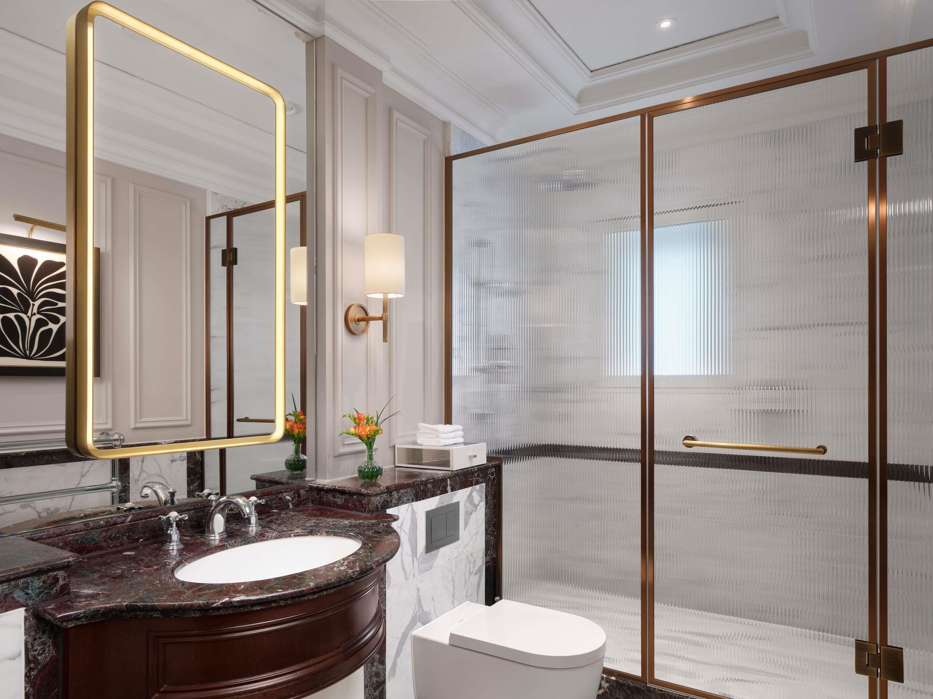 Un baño moderno con tocador de mármol, un espejo grande, cabina de ducha de vidrio y un inodoro blanco.