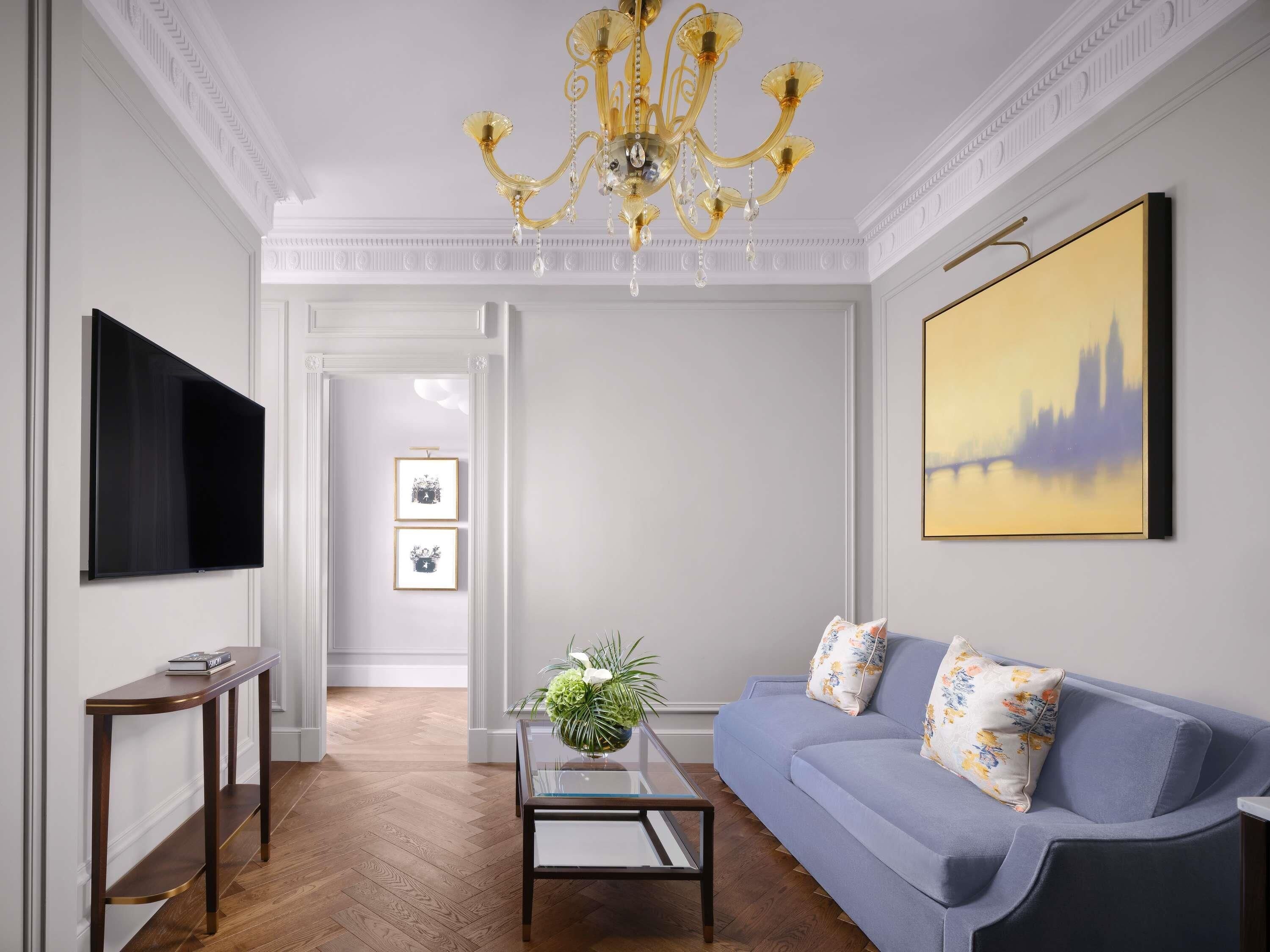 A living room with a flat-screen TV, a blue sofa, a glass coffee table, and a chandelier.