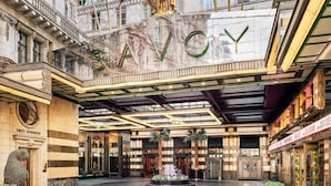 A grand interior with the word "SAVOY" prominently displayed on a reflective wall, surrounded by classical architectural details and flags. - The Savoy (London)