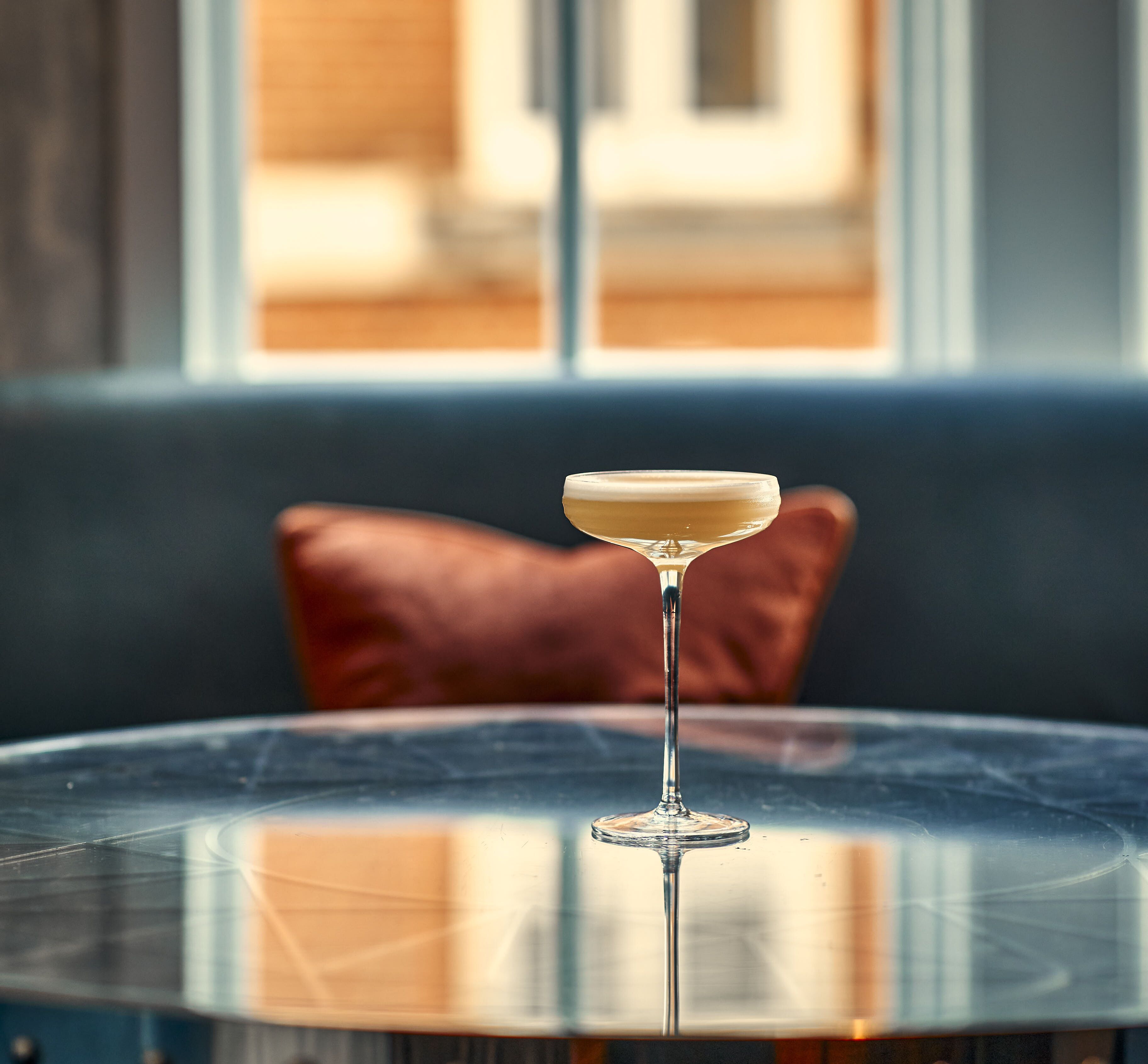 A cocktail on a glass table with a view of a building through a window.
