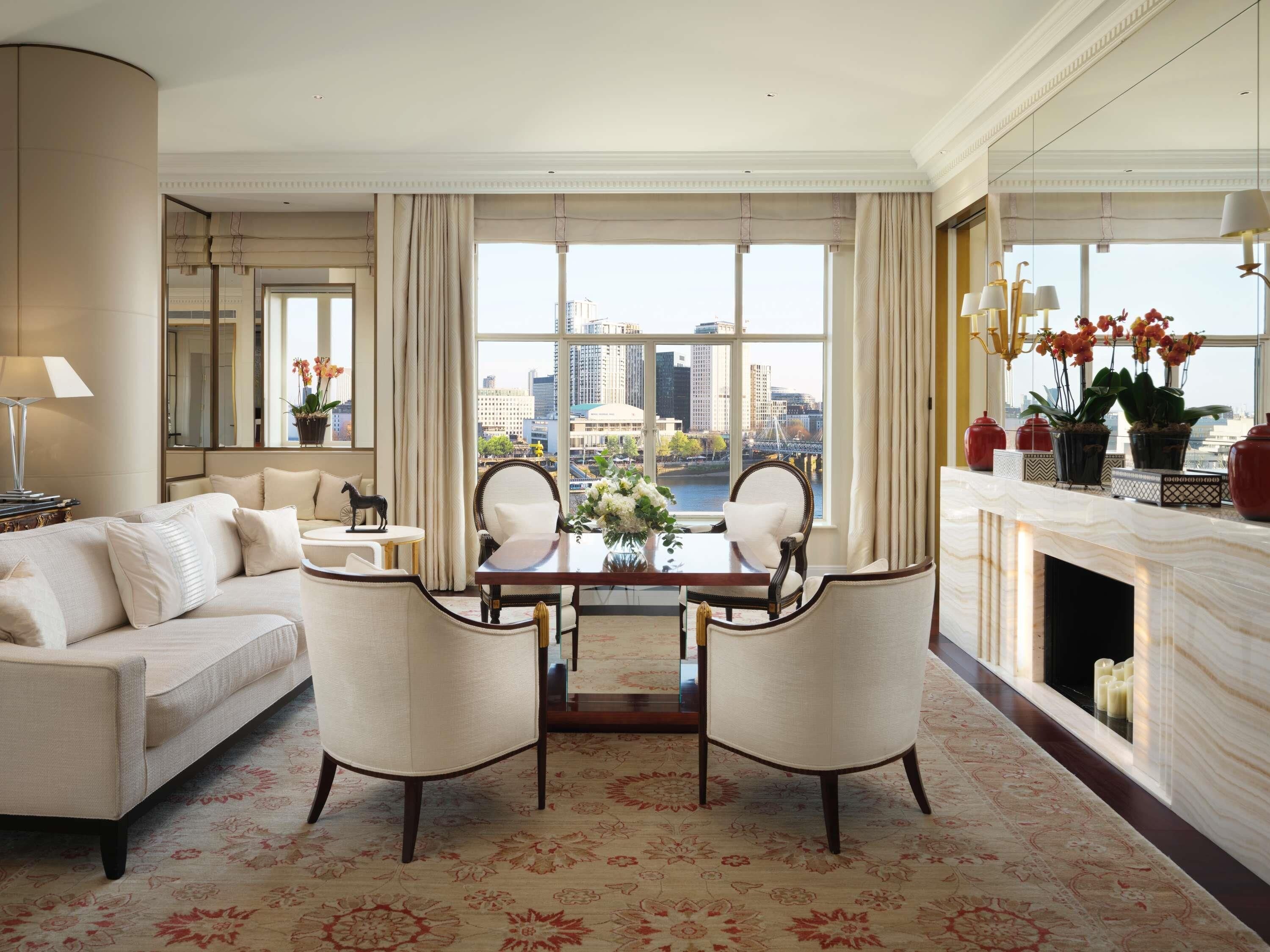 A spacious living room with a large window offering a city view, a fireplace, and a dining area with two chairs and a table.