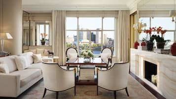 A spacious living room with a large window offering a city view, a fireplace, and a dining area with two chairs and a table.