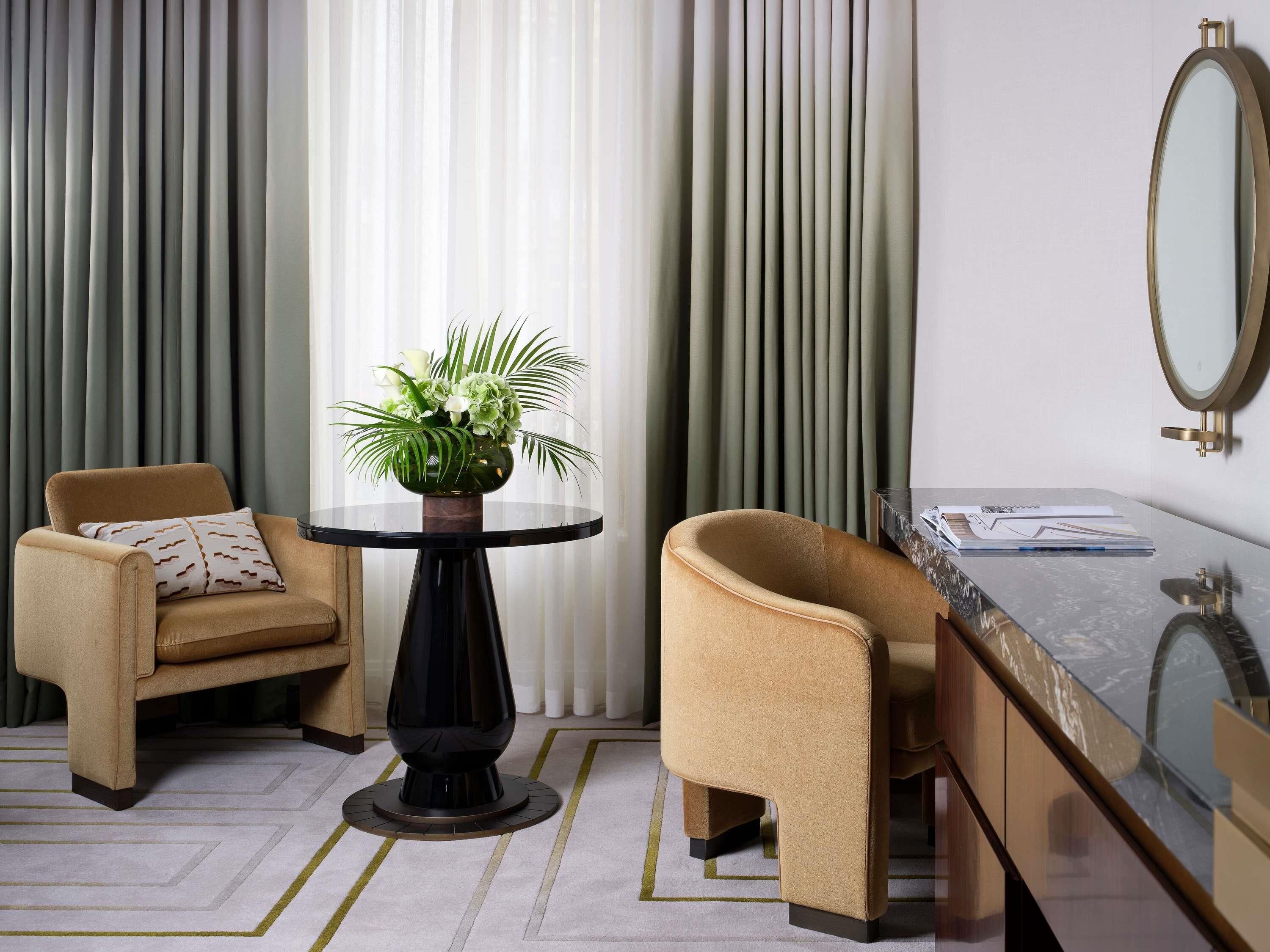 Quarto moderno com uma mesa redonda, duas poltronas, um espelho e um vaso com flores.