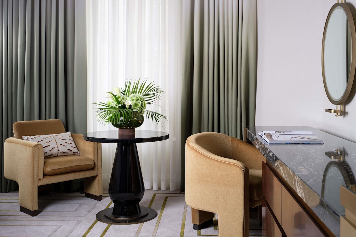 A modern room with a round table, two armchairs, a mirror, and a vase with flowers.