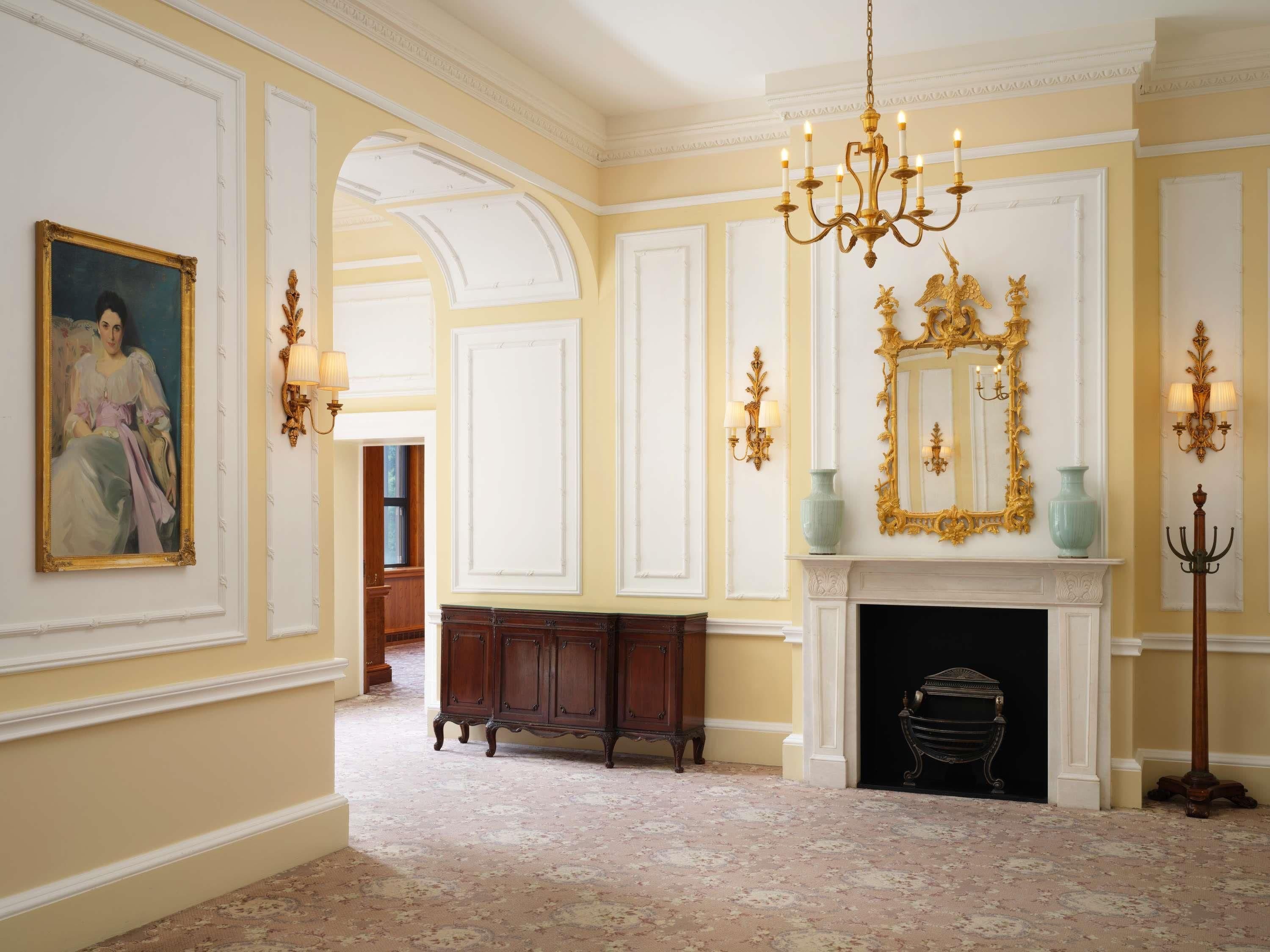 A room with a chandelier, a fireplace, a large mirror, and a painting on the wall.