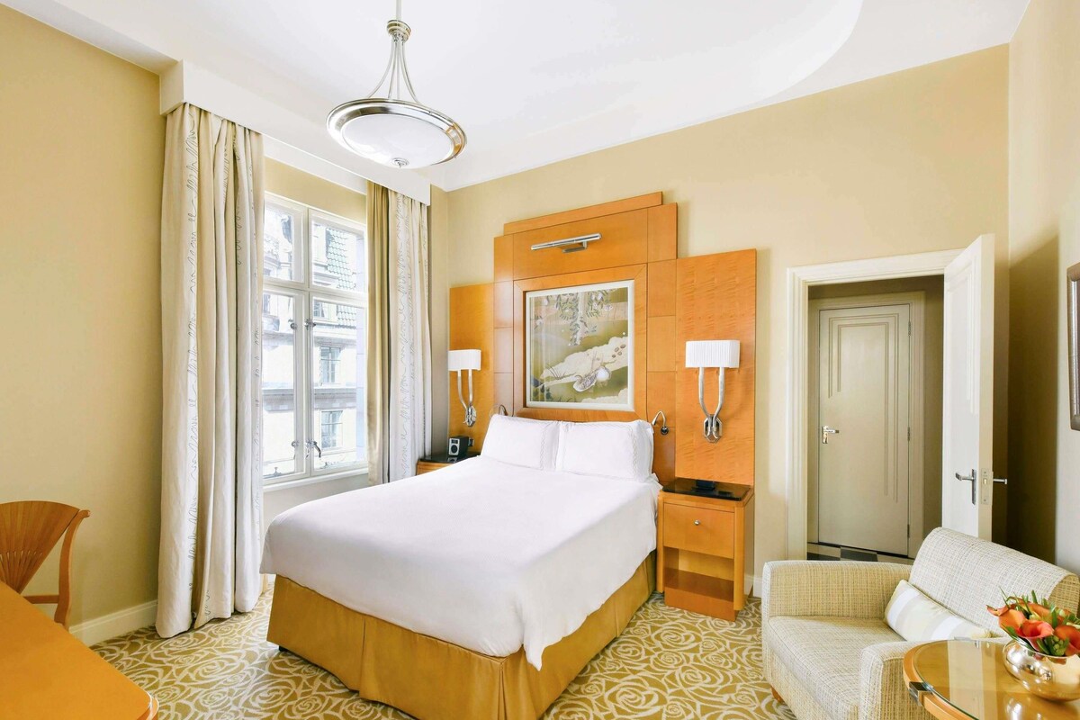 A hotel room with a large bed, a sofa, a desk, and a painting on the wall.