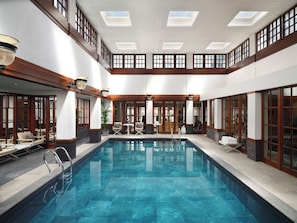 A large indoor swimming pool with a tiled floor, surrounded by seating areas and a bar.