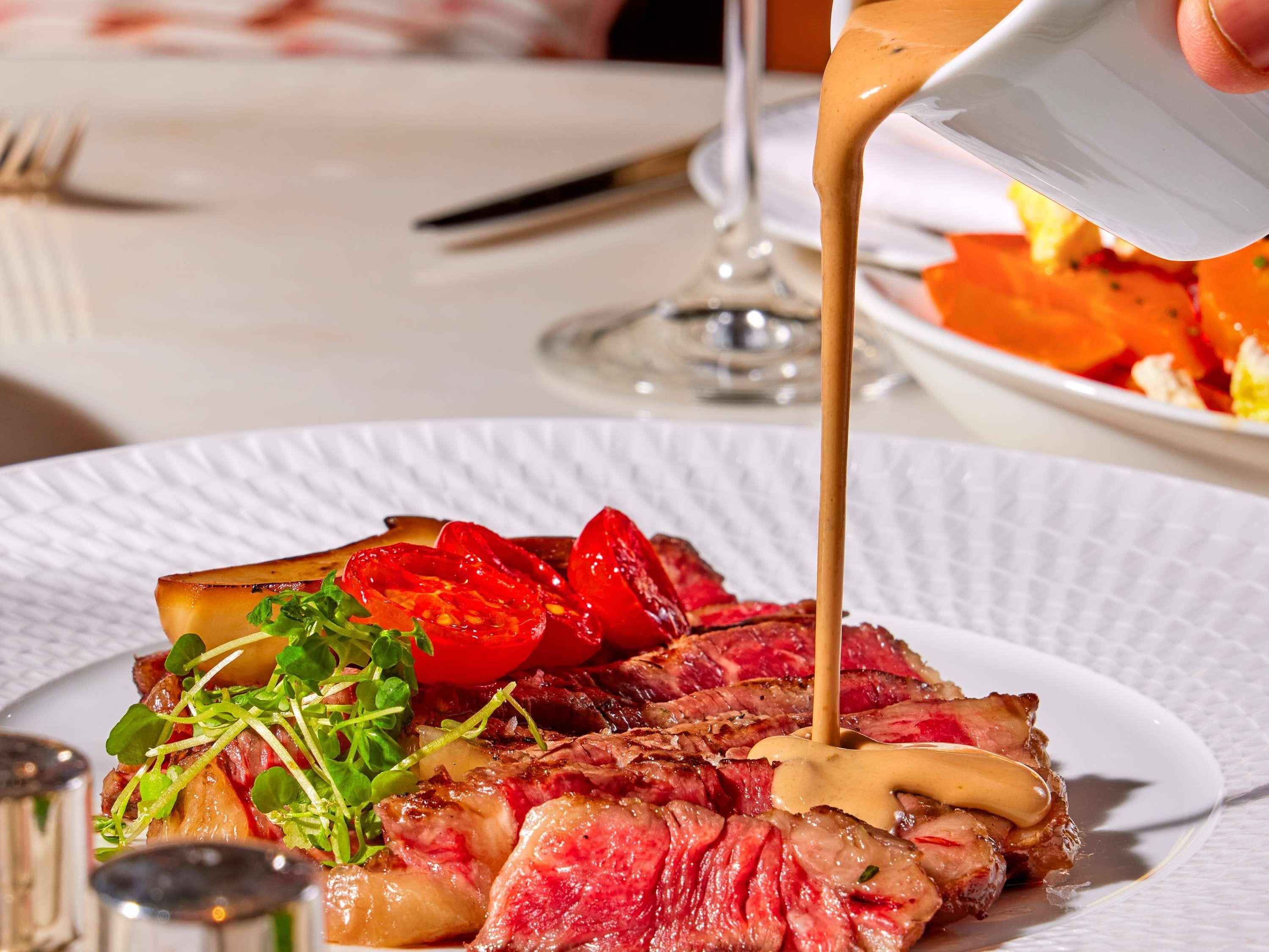 A plate of steak with a creamy sauce being poured over it.