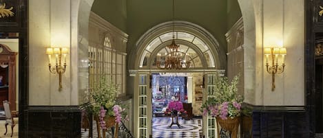 Um hall imponente com pisos de mármore, um candelabro e arandelas.