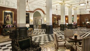 Un amplio vestíbulo con techos altos, columnas decorativas y un suelo a cuadros.
