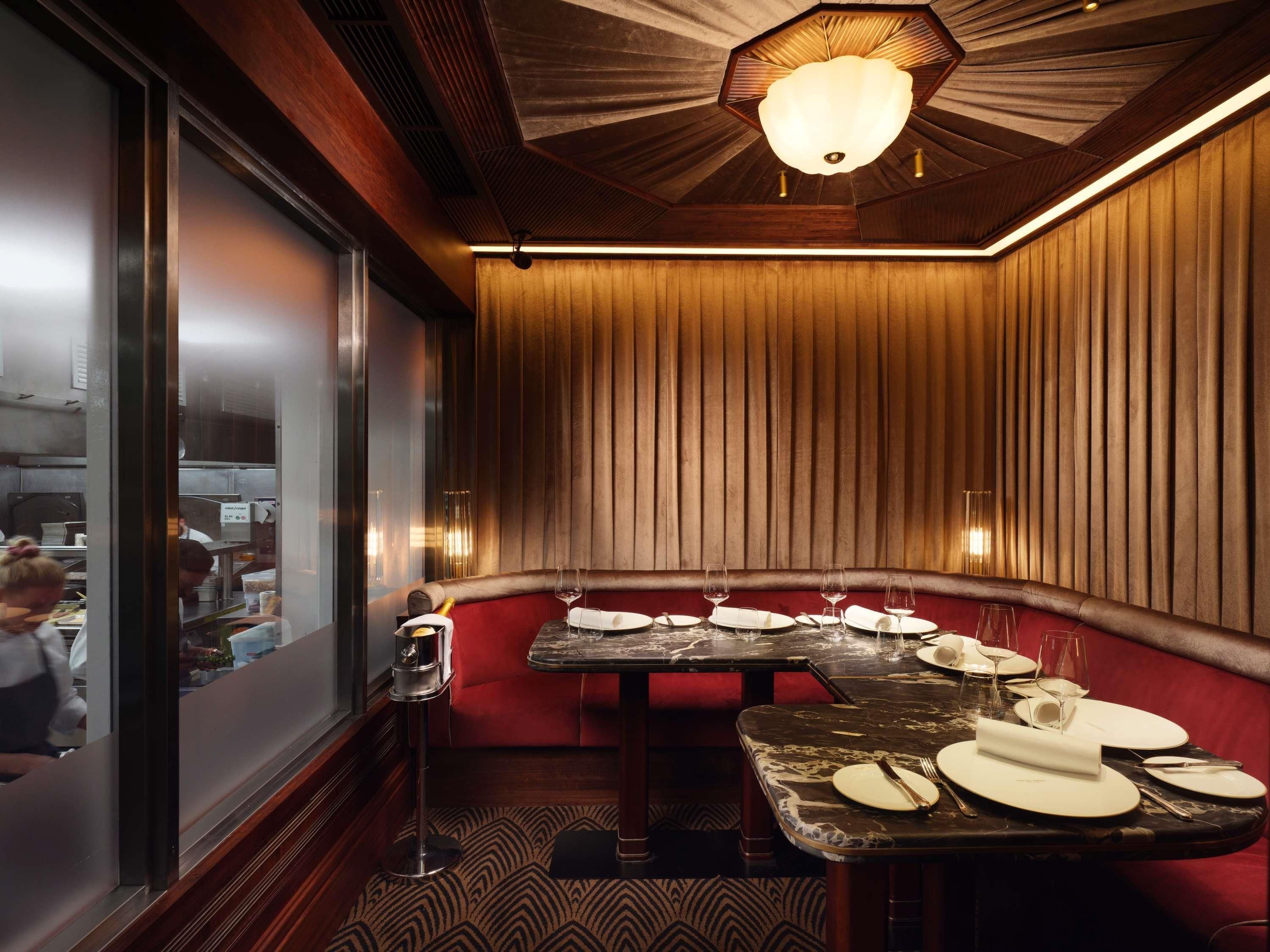 Un restaurante con una zona de asientos tipo cabina, techo de madera y vistas a la cocina a través de un mamparo de vidrio.