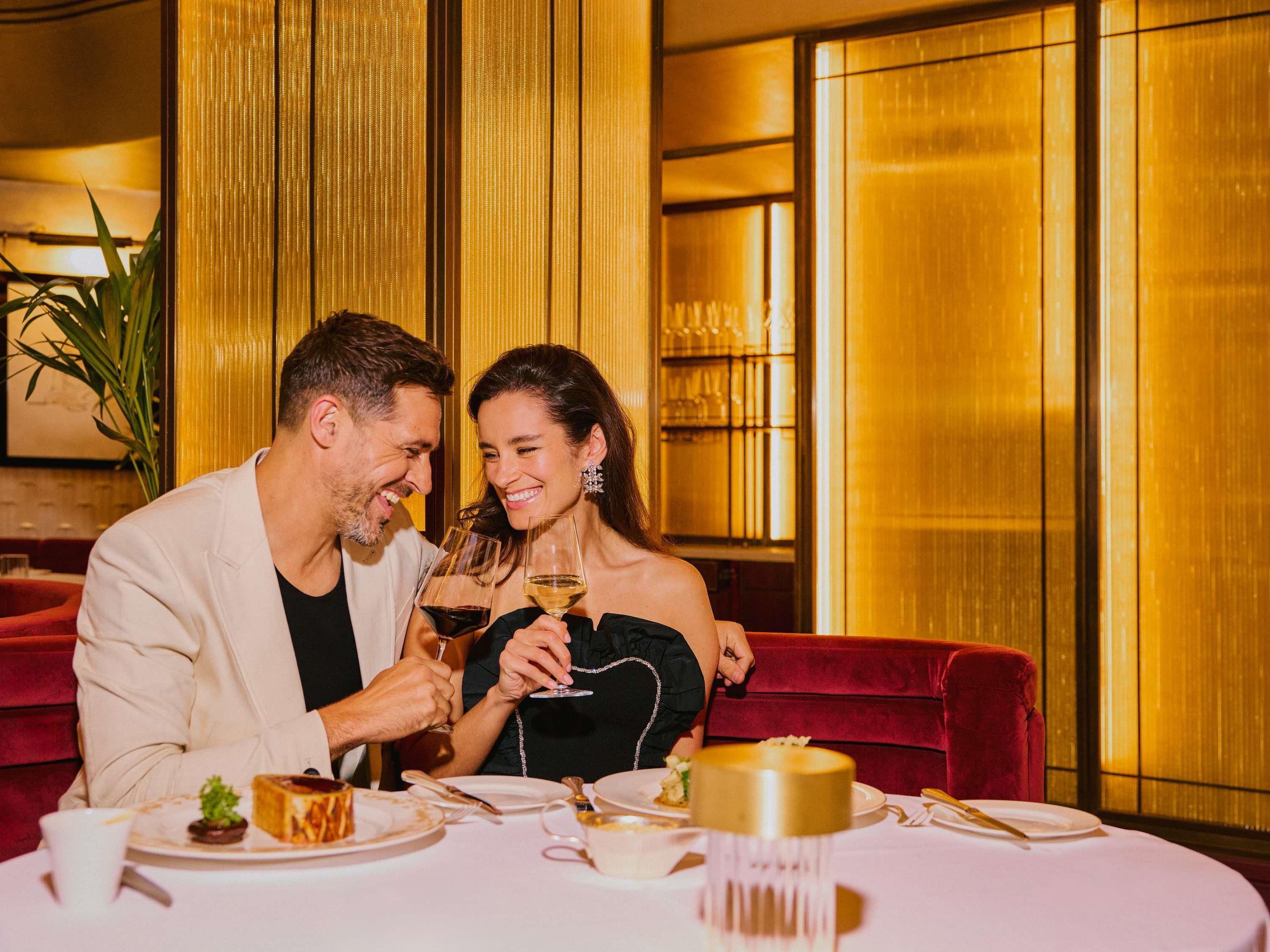 Una pareja sentada a una mesa con un postre, copas de vino y un centro de mesa dorado.
