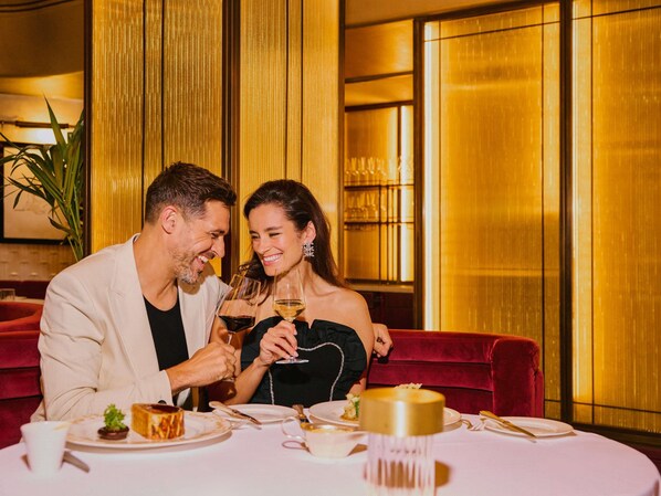 A couple seated at a table with a dessert, wine glasses, and a gold-colored centerpiece.