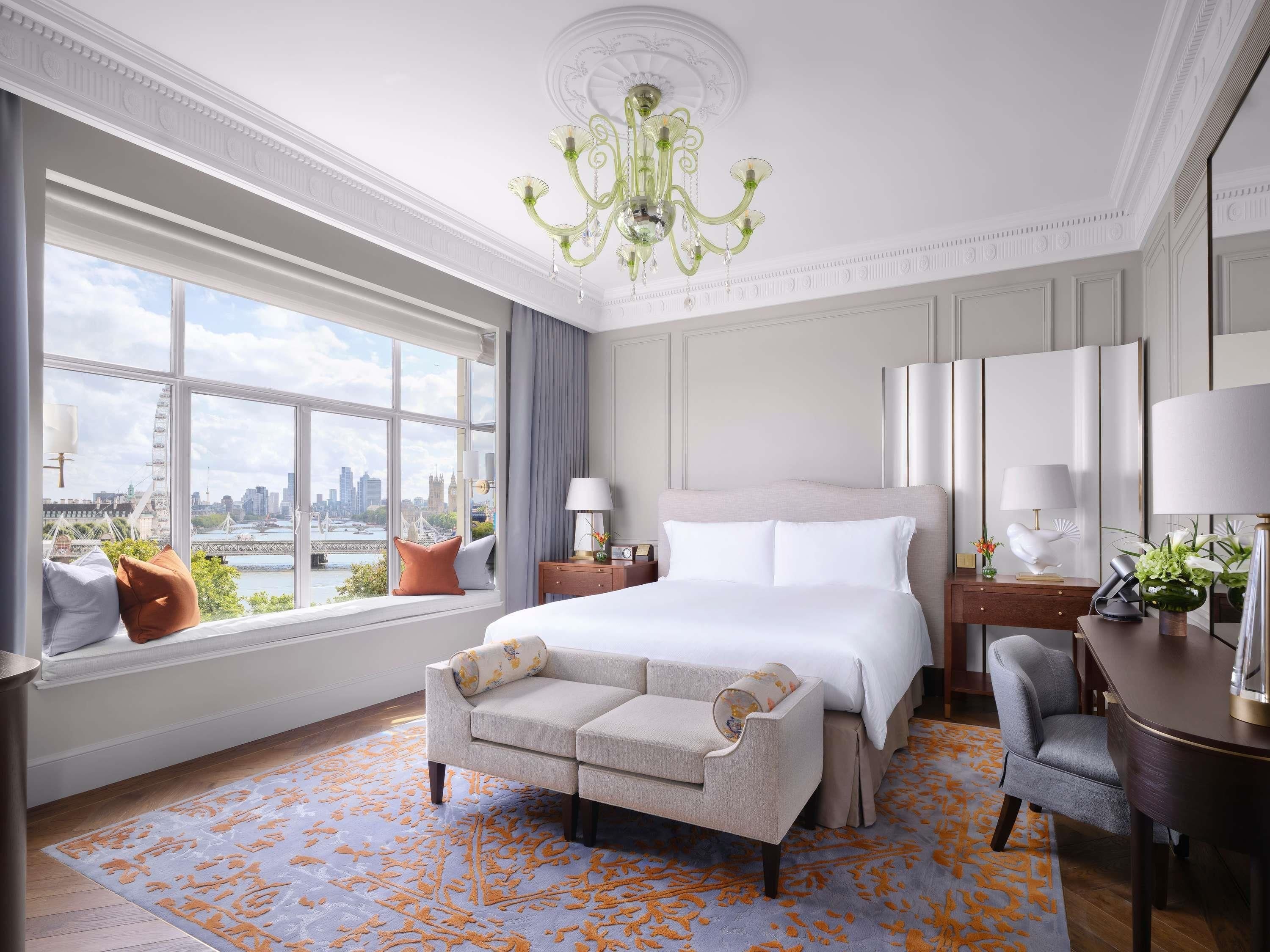 Ein Hotelzimmer mit einem großen Bett, einer Couch, einem Schreibtisch und Blick auf die Stadt.
